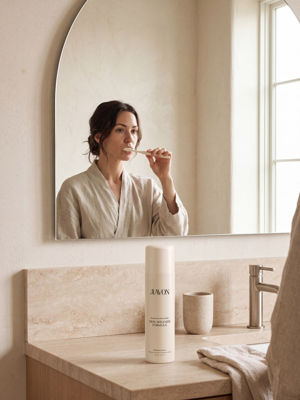 Woman brushing her teeth at an arched mirror with the JIAVON bottle on the counter